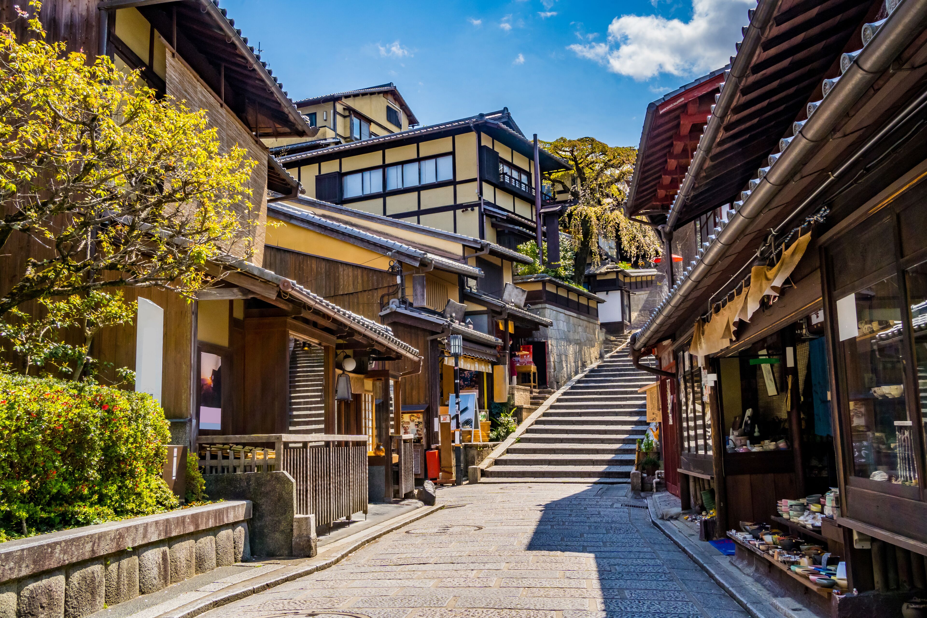 Una calle tradicional japonesa con edificios de madera, una escalera de piedra y un cielo azul despejado.