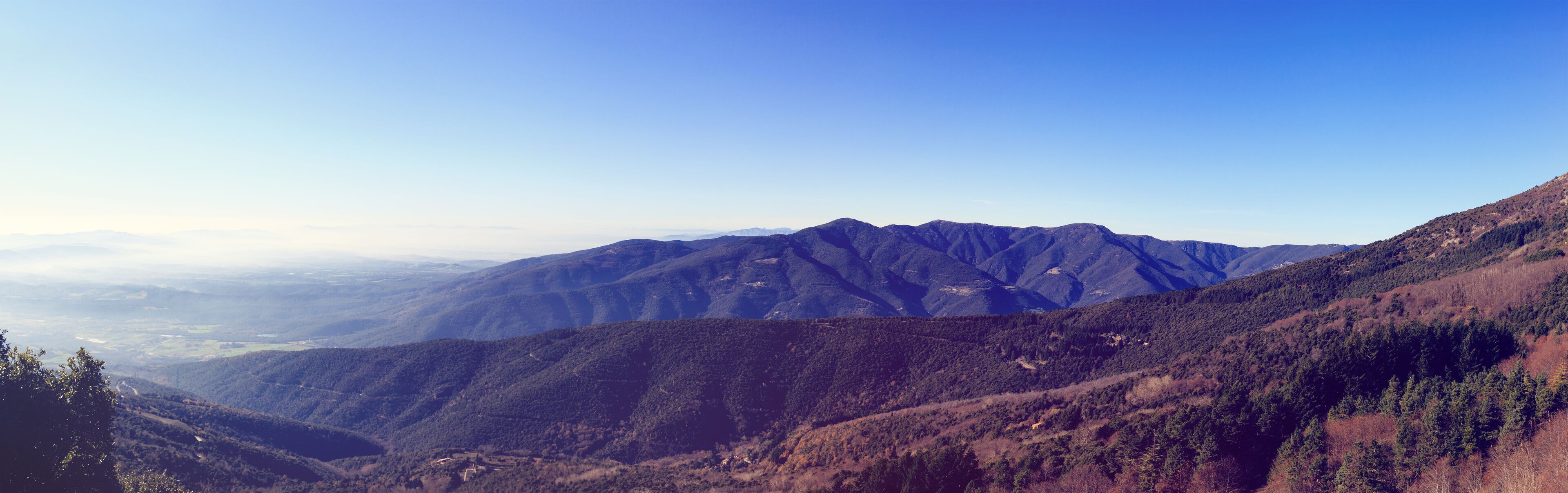 A mountainous landscape with dense forests and a clear sky.