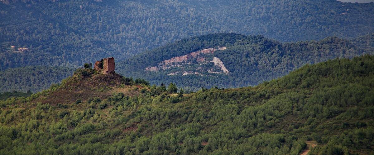 A mountainous landscape with a ruined structure on a hill and a path leading towards it.