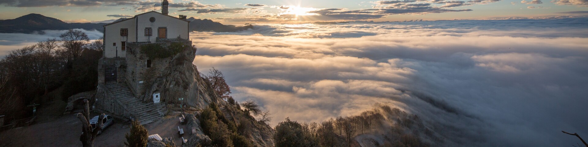 Una casa de montaña con vista a un valle cubierto de nubes al amanecer.