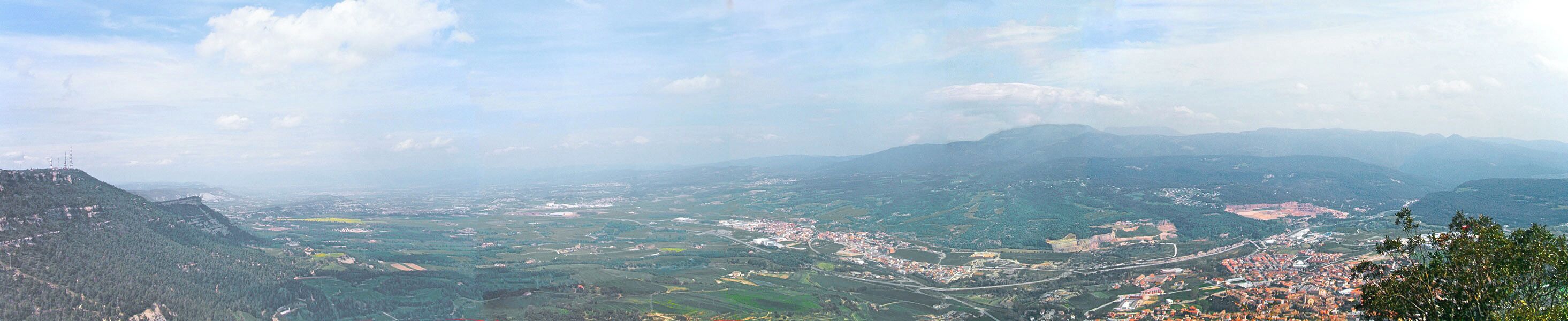 A panoramic view of a valley with a town, mountains, and a river.