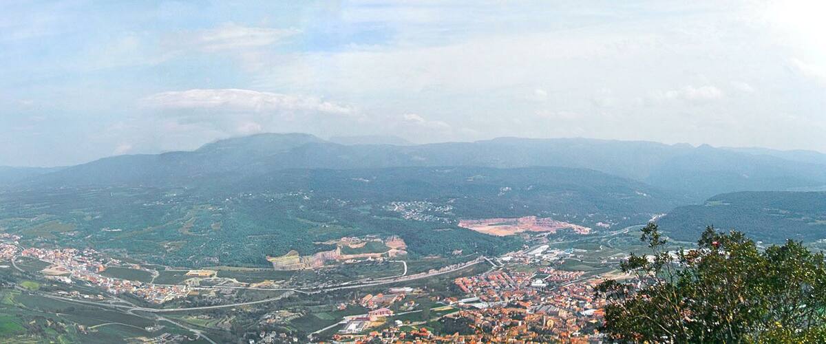 A panoramic view of a valley with a town, mountains, and a river.