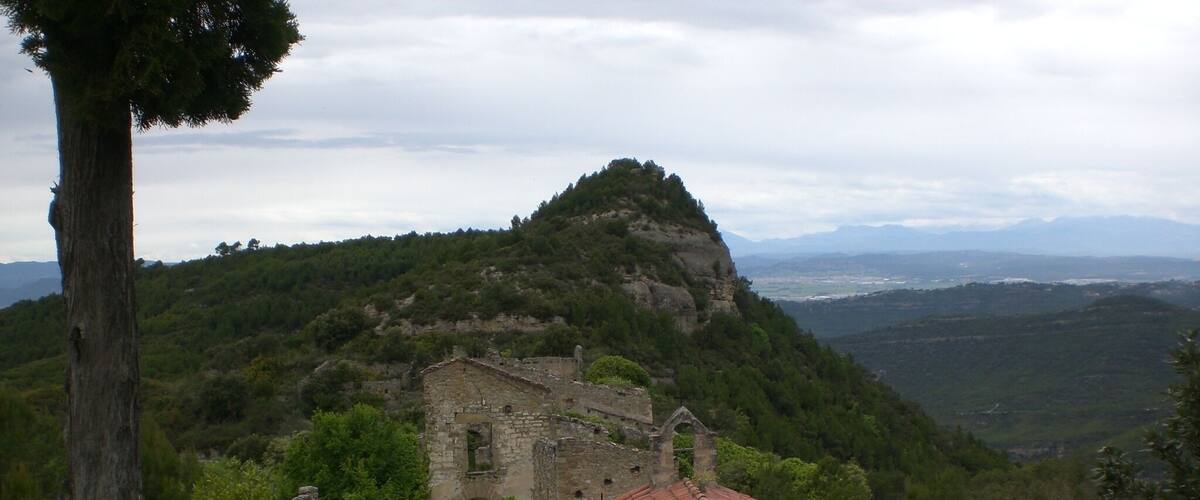 A stone church with a red-tiled roof surrounded by lush greenery and mountains in the background.