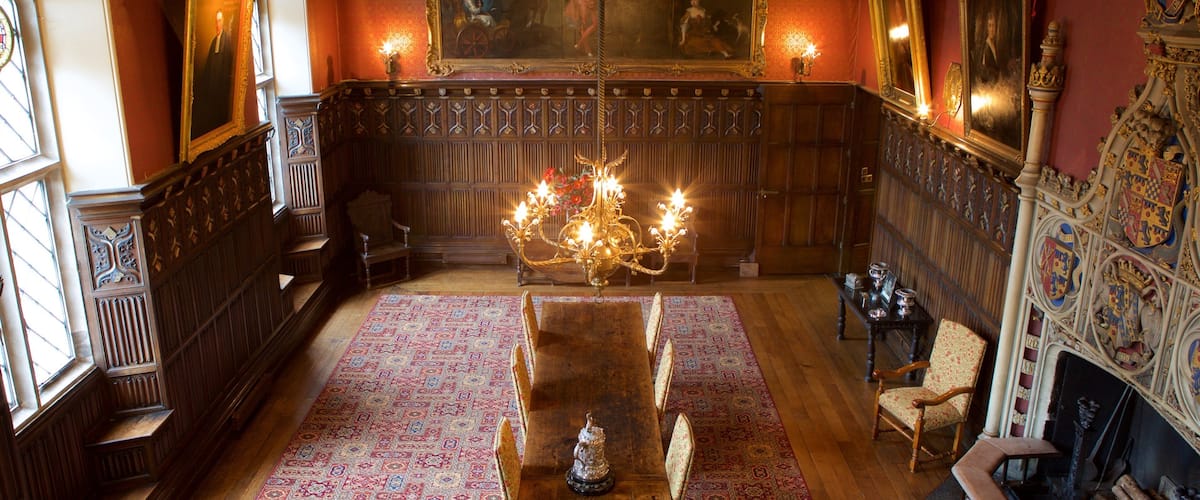 A grand room with a large chandelier, wooden paneling, and a long table.
