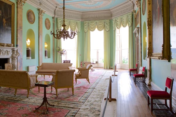 Uma sala imponente com móveis requintados, um candelabro e pinturas clássicas.
