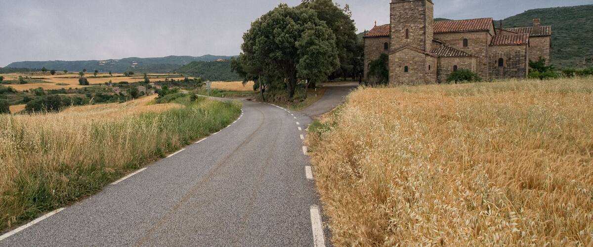 A rural road curving to the left, leading to a stone church with a bell tower.