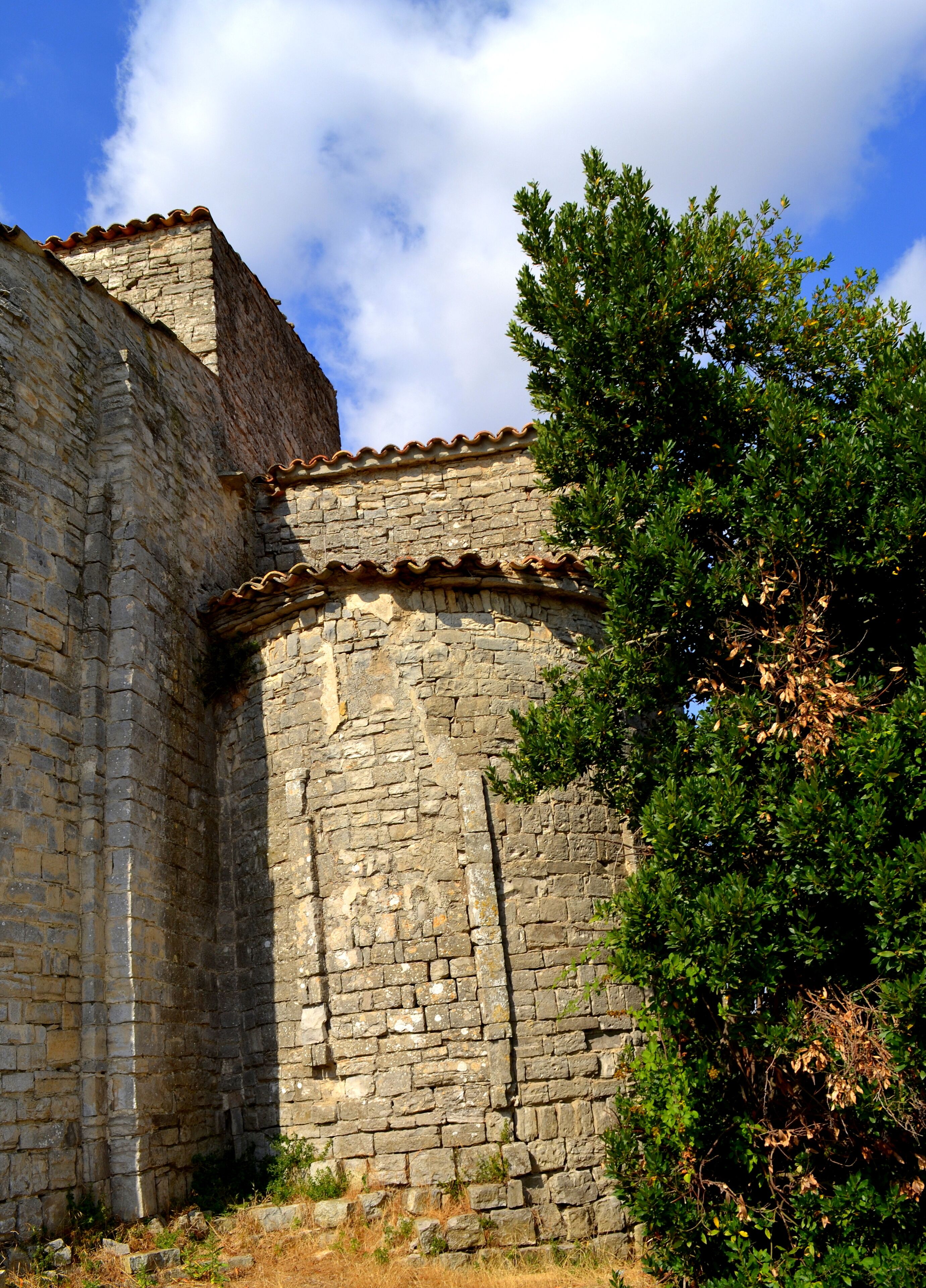 A stone building with a tiled roof and a tree in the foreground.