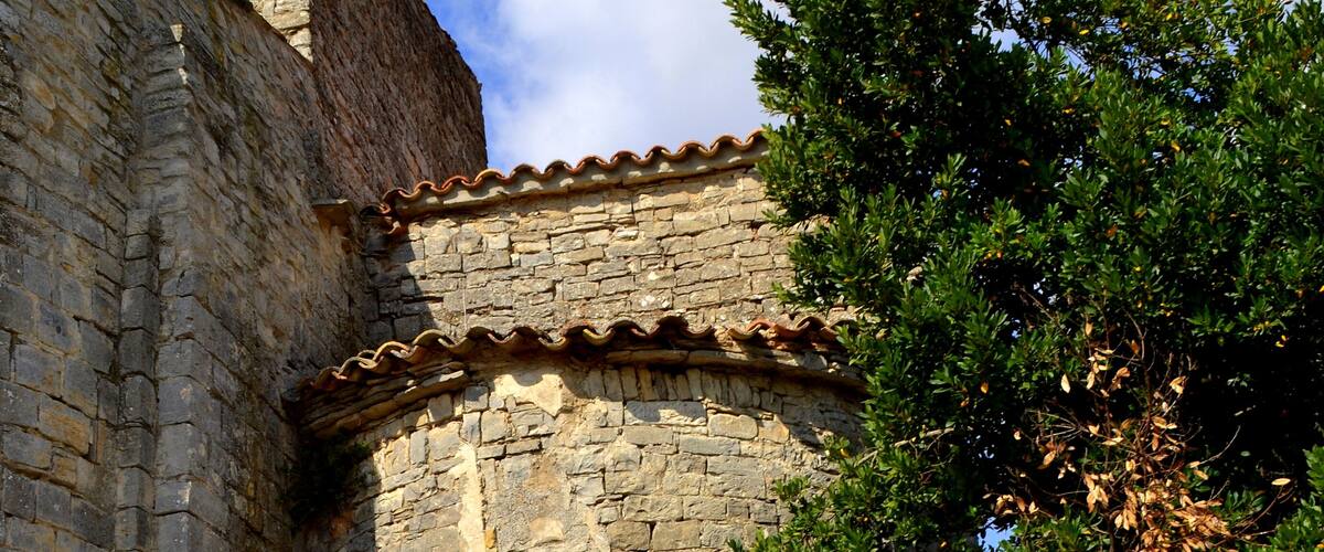 A stone building with a tiled roof and a tree in the foreground.