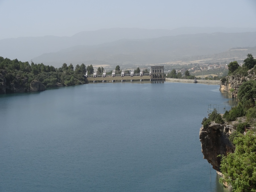 A large dam with multiple turbines on a river surrounded by hills and trees.
