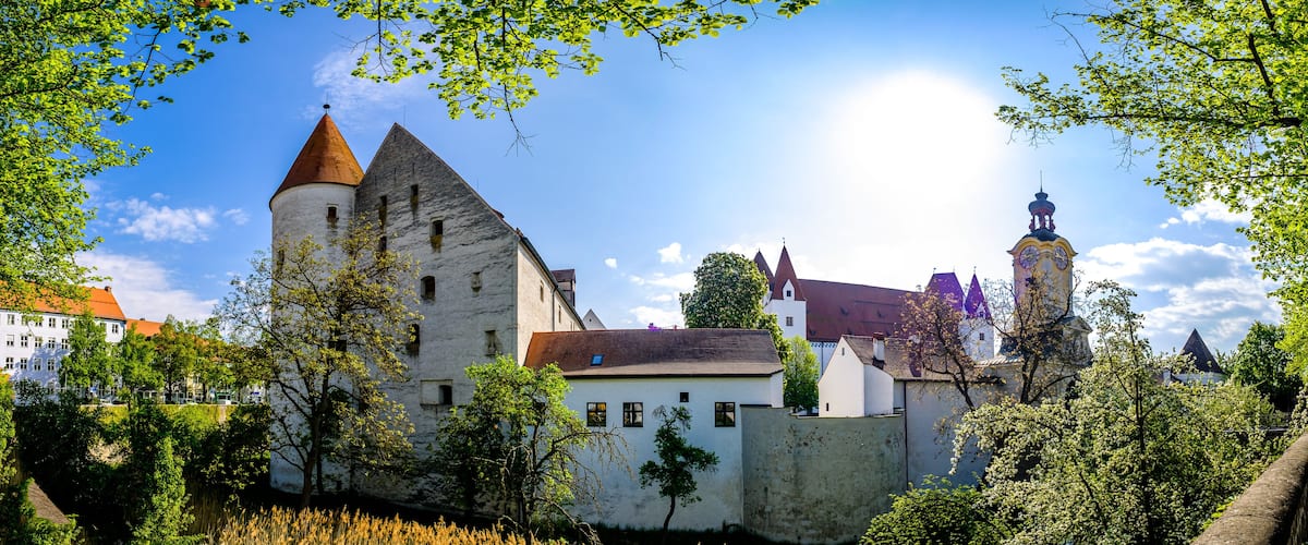 A historic castle with a prominent tower and a clock tower, surrounded by lush greenery and a clear blue sky.