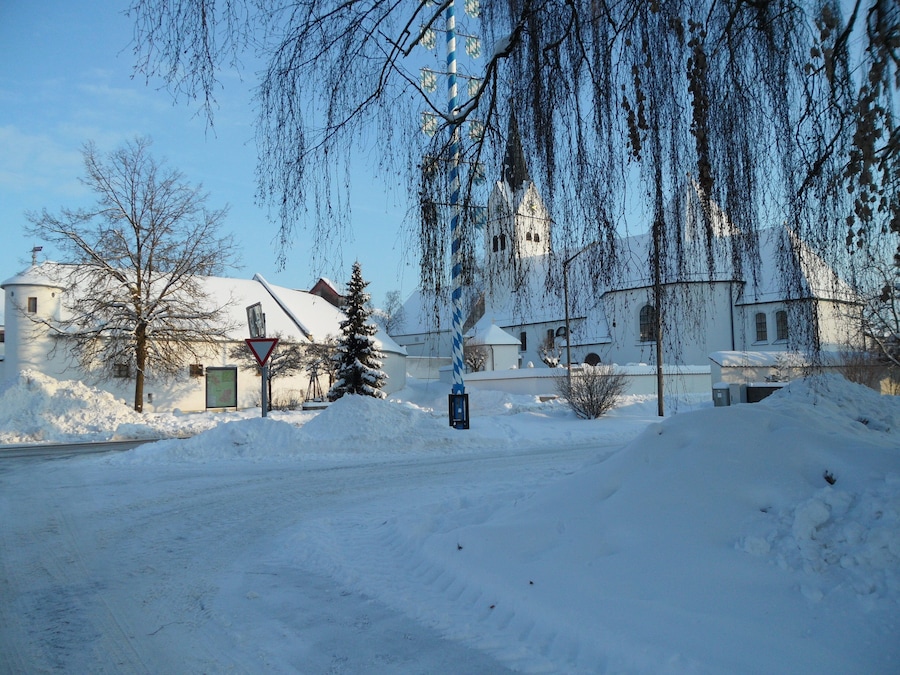 A snow-covered landscape with a church, bare trees, and a road.