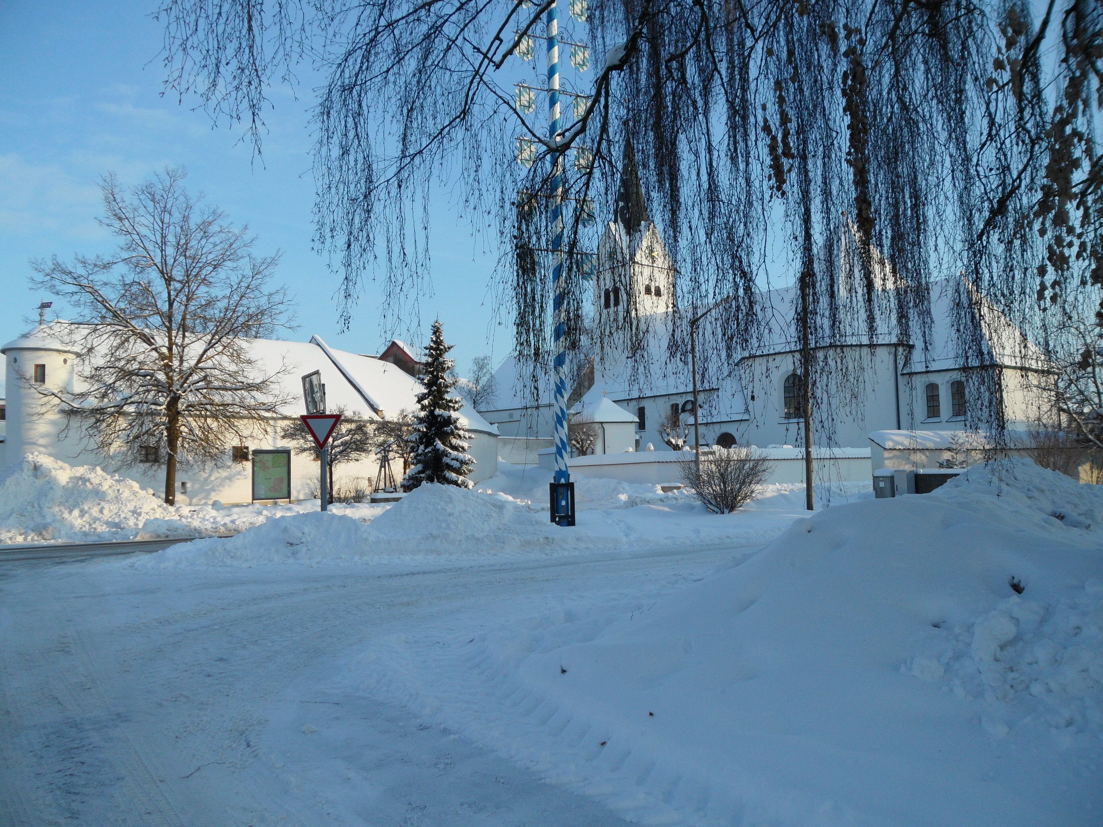 A snow-covered landscape with a church, bare trees, and a road.