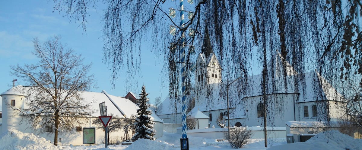 A snow-covered landscape with a church, bare trees, and a road.