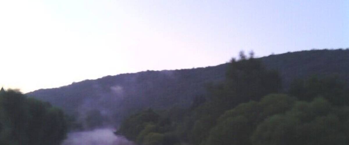 A calm river reflecting trees and hills.