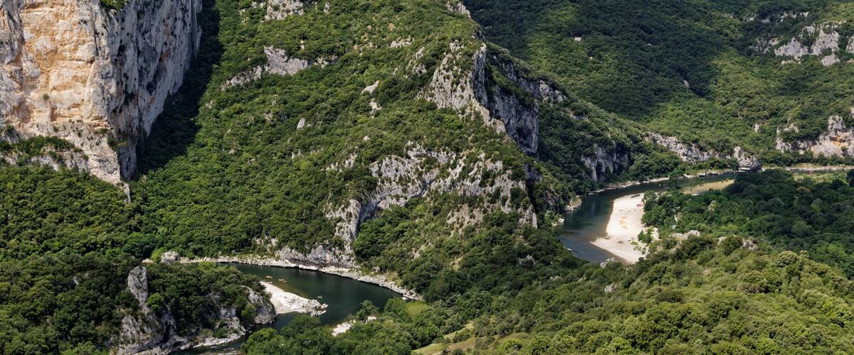 Un fiume serpeggia attraverso un paesaggio montuoso, caratterizzato da scogliere e una vegetazione rigogliosa.