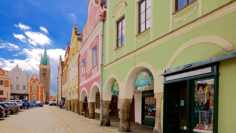 A cobblestone street lined with colorful historic buildings, a church spire, and a pizza restaurant.