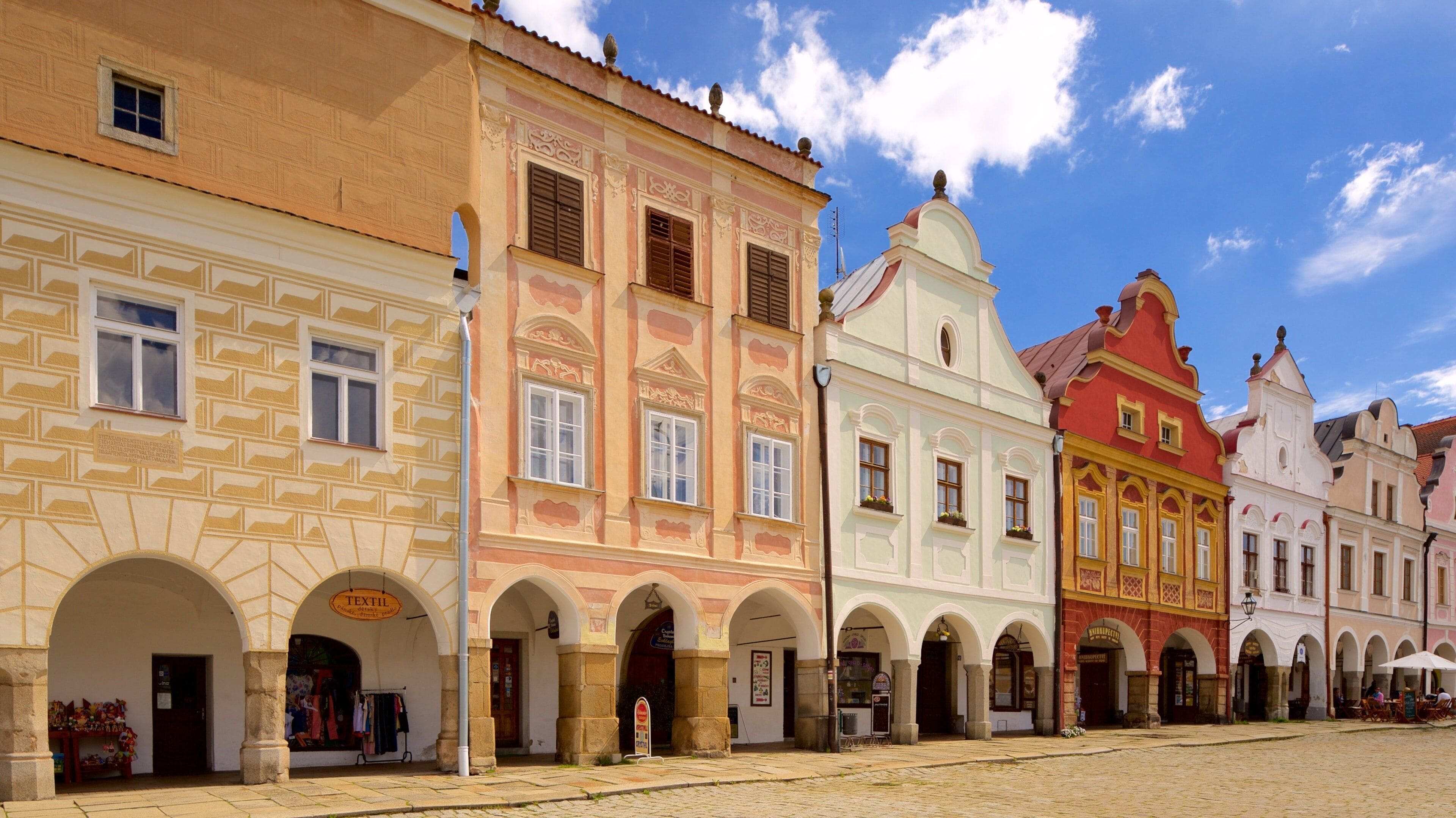 A historic European street with colorful buildings, arches, and cobblestone pavement.