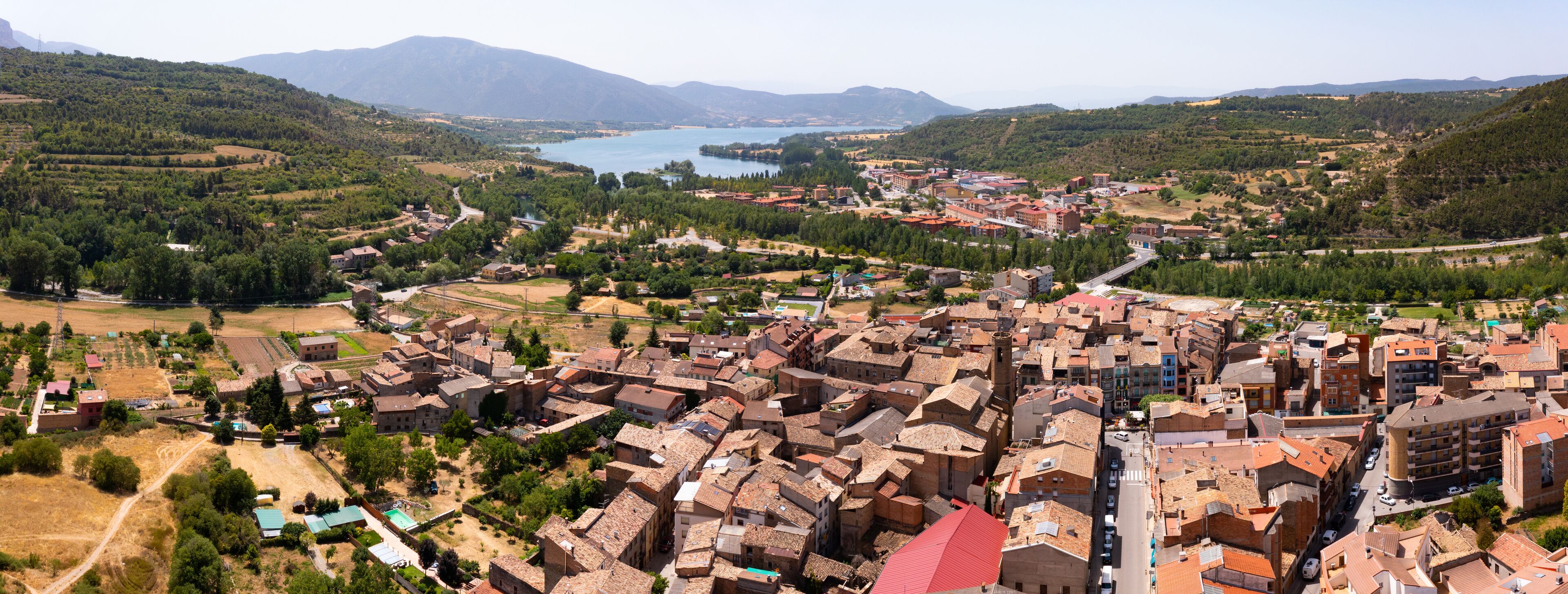 A town with a river, mountains, and a mix of traditional and modern buildings.