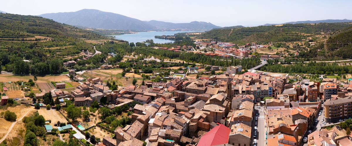A town with a river, mountains, and a mix of traditional and modern buildings.