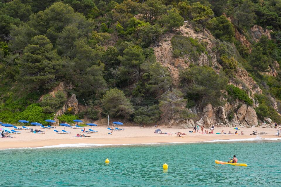 Una spiaggia con ombrelloni blu, persone che si prendono il sole e una scogliera sullo sfondo.
