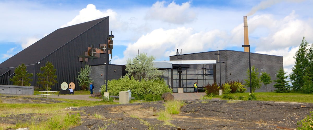 A modern building with a large black roof and a tall chimney emitting smoke.