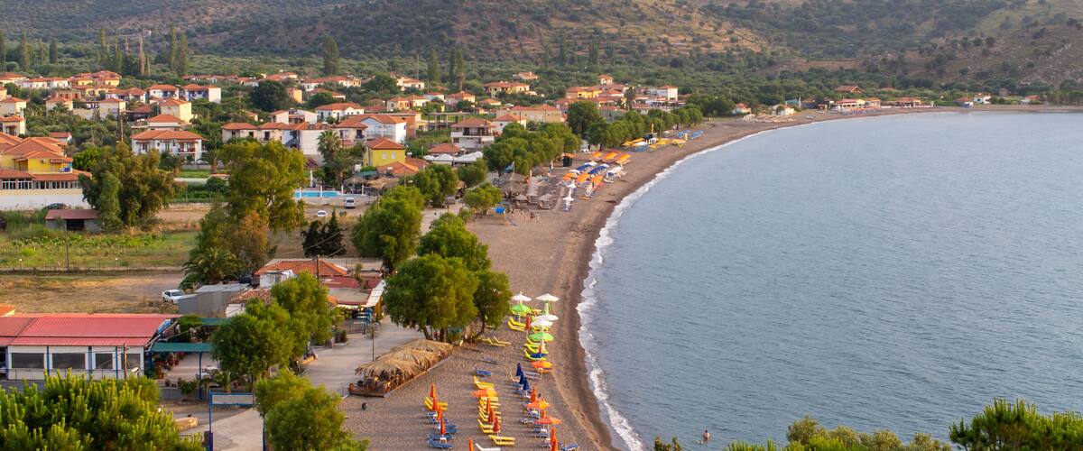 A coastal town with a beach, houses, and mountains in the background.