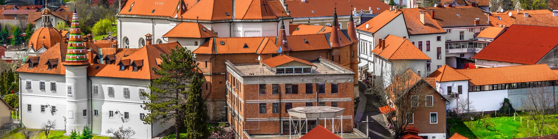 A historic town with a prominent church tower, red-roofed buildings, and lush green hills in the background.