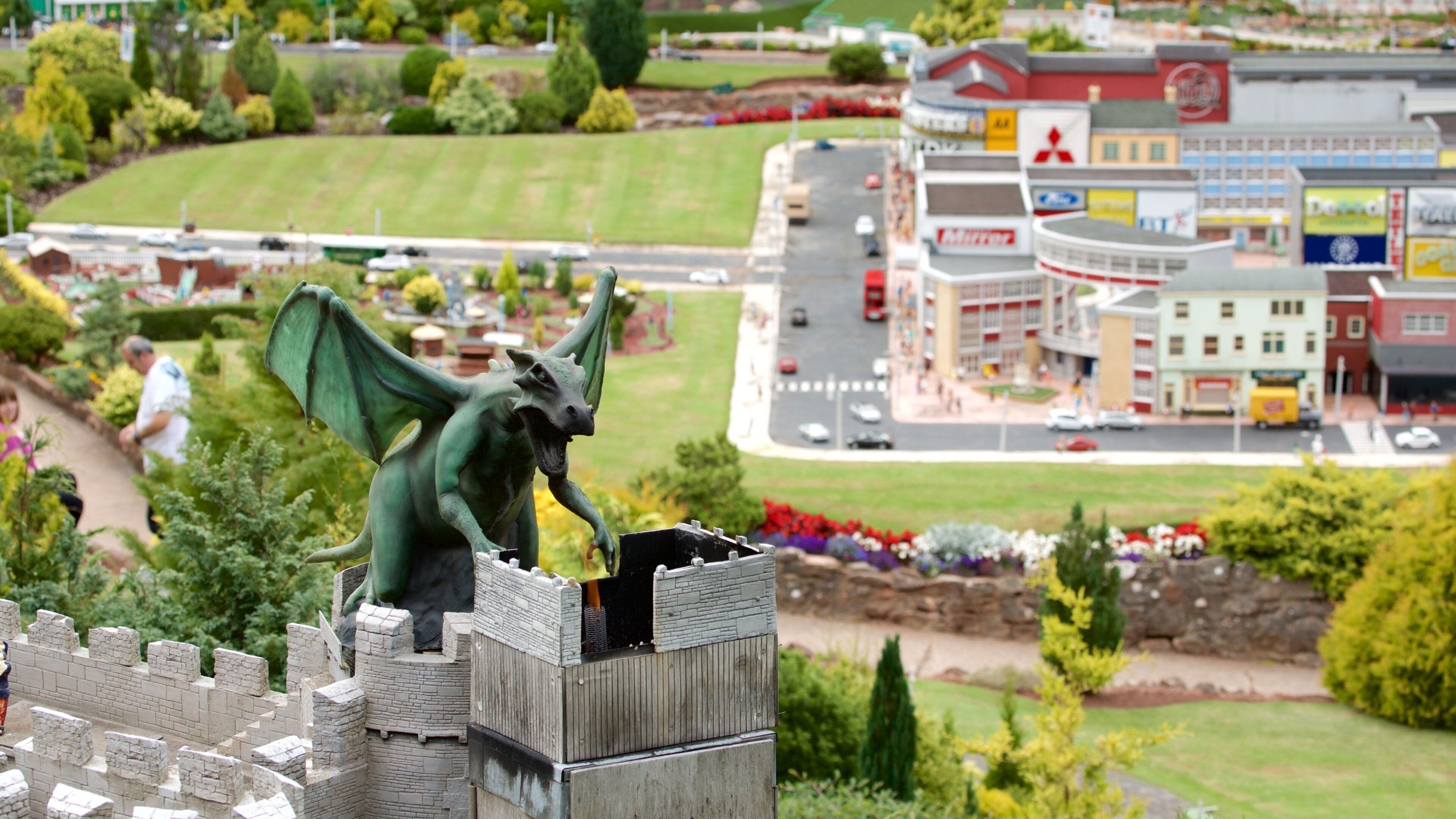 Une statue de dragon sur le sommet d’un mur de château, un parking et une zone commerciale avec divers magasins.