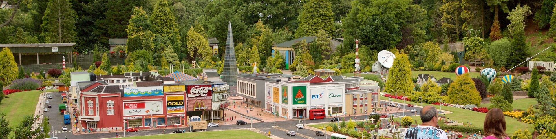 A model town with various buildings, a green field, and a hill with two people observing.