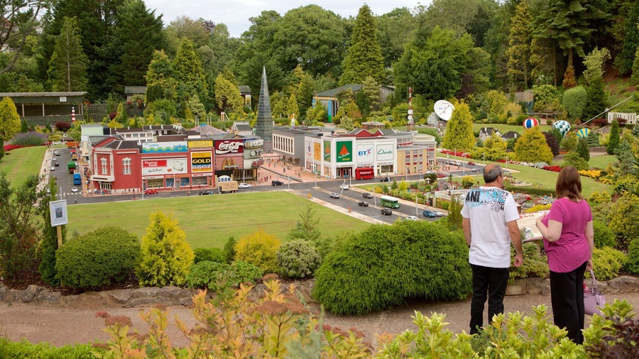 A model town with various buildings, a green field, and a hill with two people observing.