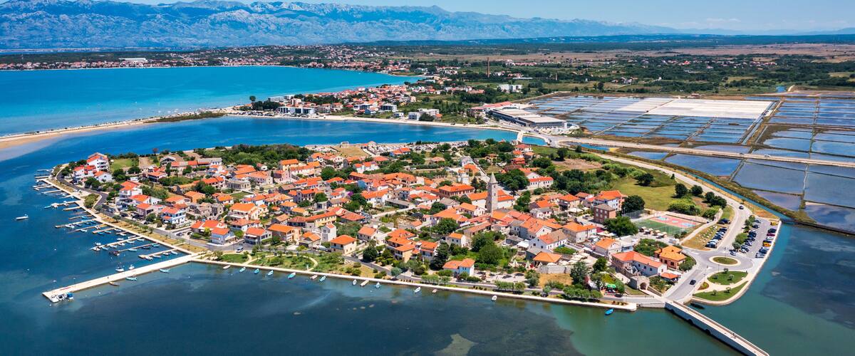 An aerial view of a coastal town with a marina, surrounded by mountains and a large body of water.