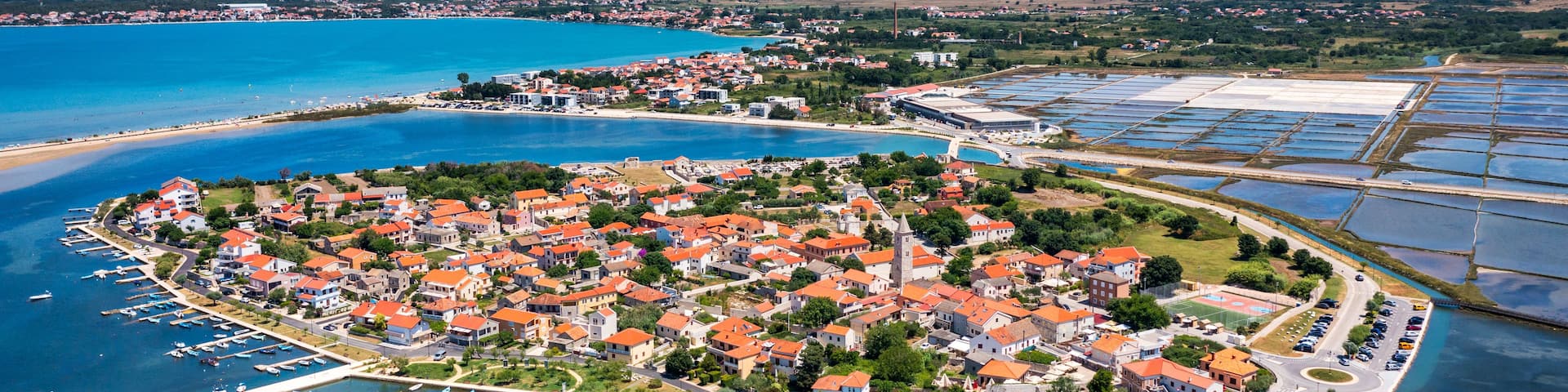 An aerial view of a coastal town with a marina, surrounded by mountains and a large body of water.