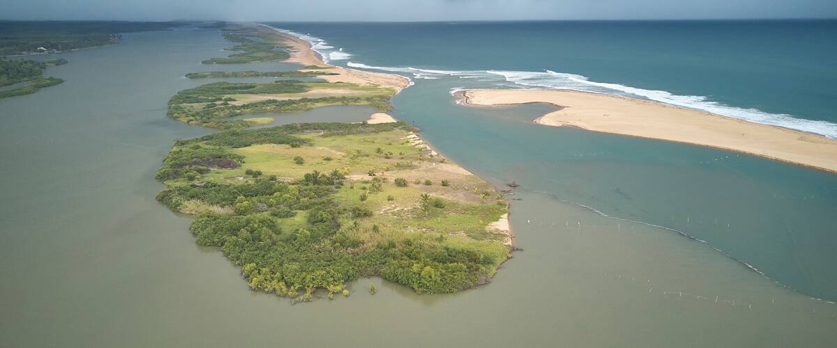 An aerial view of a coastal landscape with a long stretch of beach, a river or lagoon, and a stormy sky.