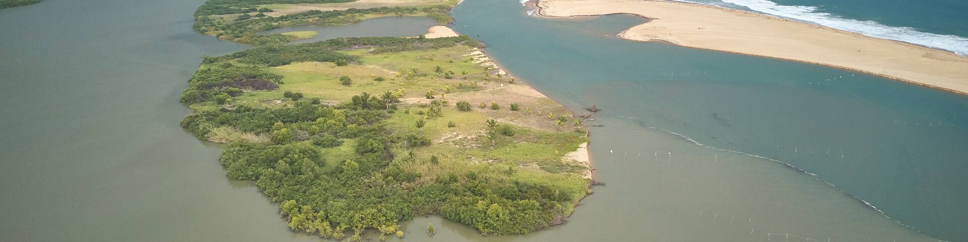 An aerial view of a coastal landscape with a long stretch of beach, a river or lagoon, and a stormy sky.