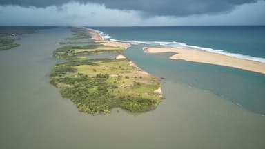 An aerial view of a coastal landscape with a long stretch of beach, a river or lagoon, and a stormy sky.
