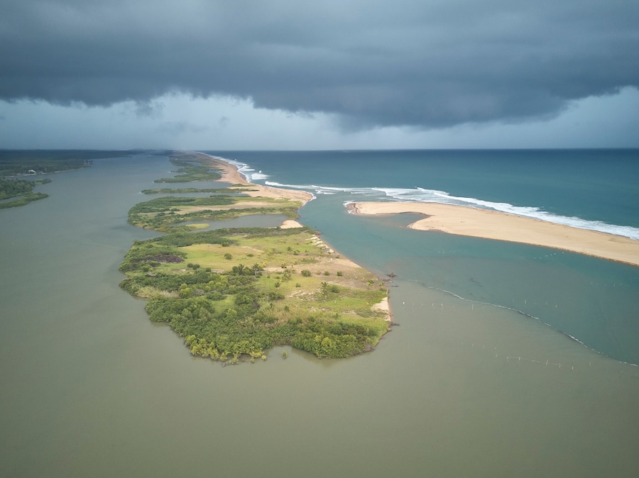 Vue aĂ©rienne dâun paysage cĂŽtier avec une longue Ă©tendue de plage, une riviĂšre ou un lagon, et un ciel orageux.