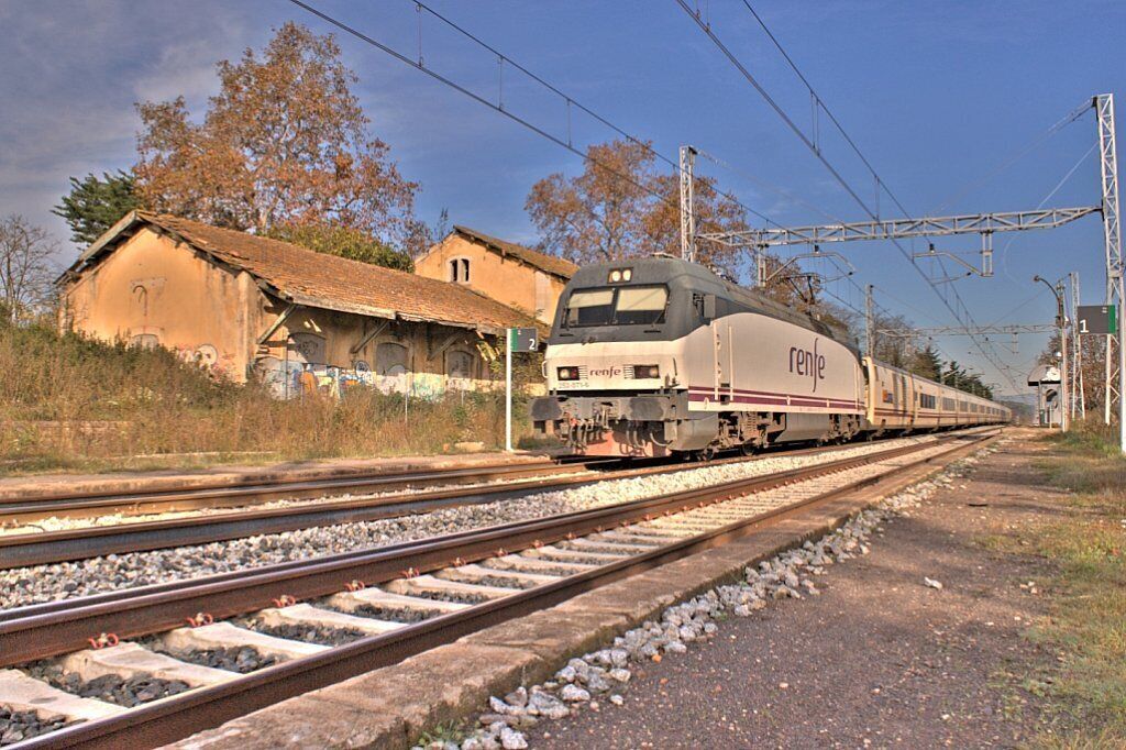 A train on tracks with a building and trees in the background.