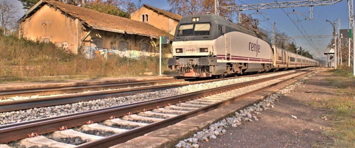 A train on tracks with a building and trees in the background.
