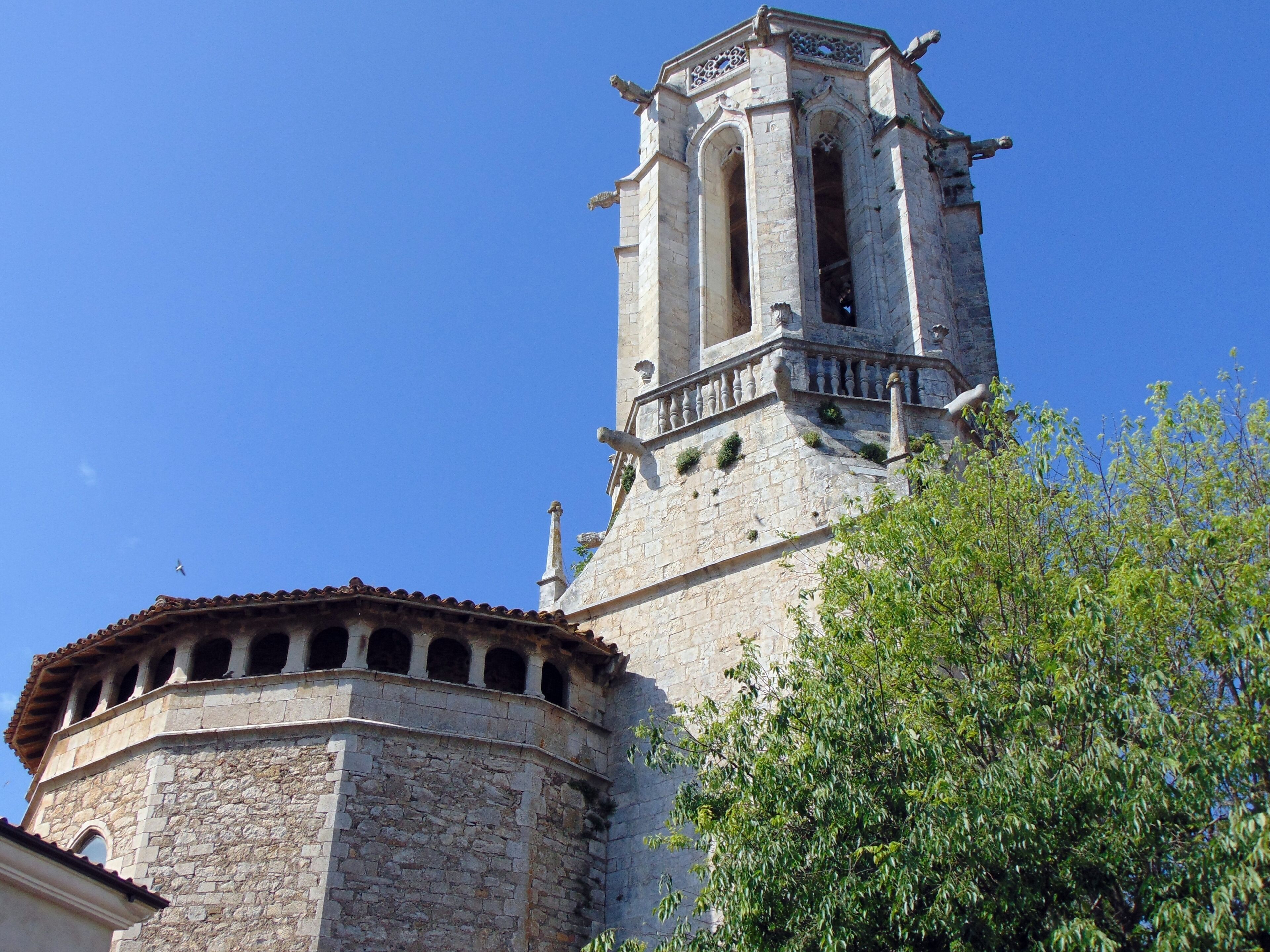 A historic tower with a bell, surrounded by stone walls and a tree.