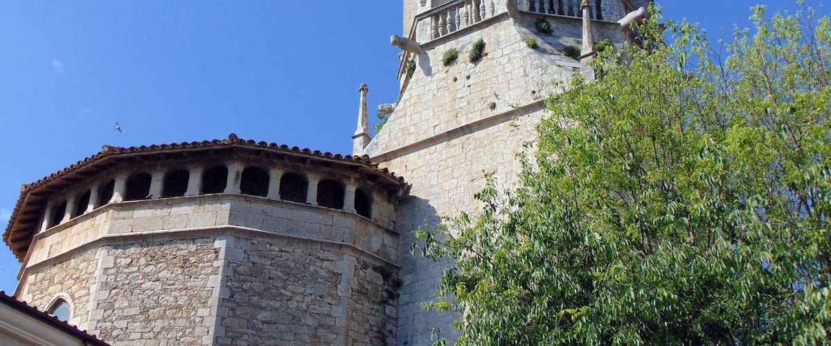 A historic tower with a bell, surrounded by stone walls and a tree.