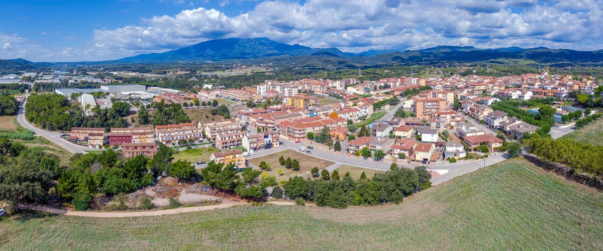 A town with red-roofed buildings, surrounded by green fields and mountains in the background.