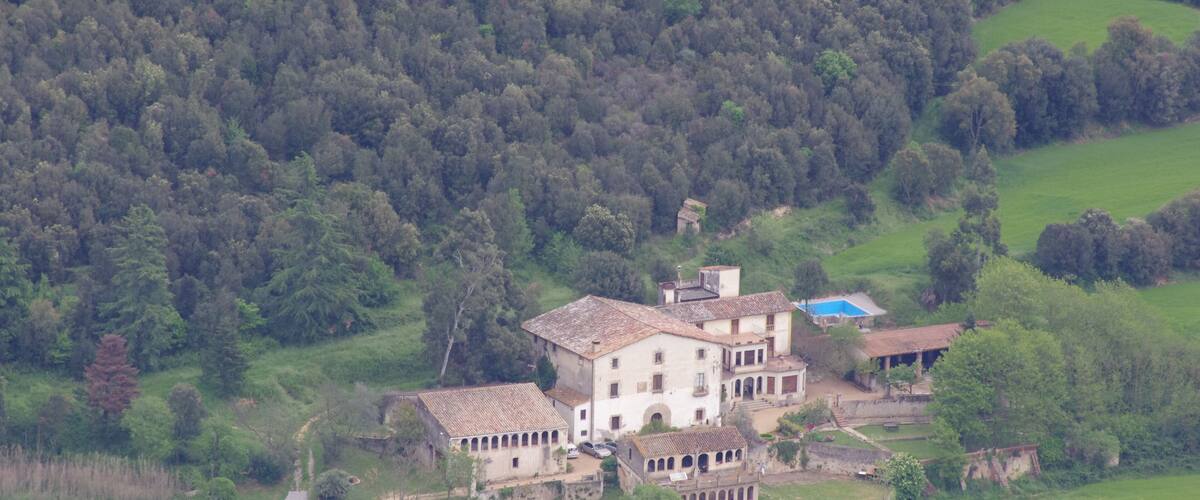 A large, historic house surrounded by lush greenery and rolling hills.