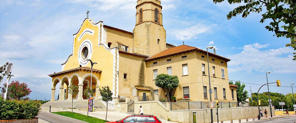 A church with a bell tower and a red car parked in front.