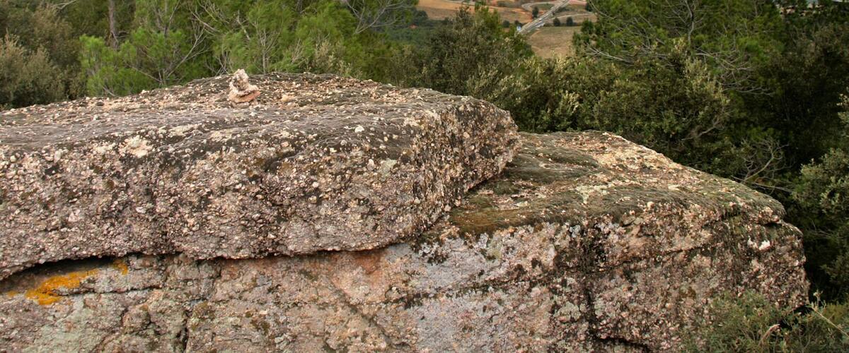A rocky outcrop with a view of a valley and distant hills.