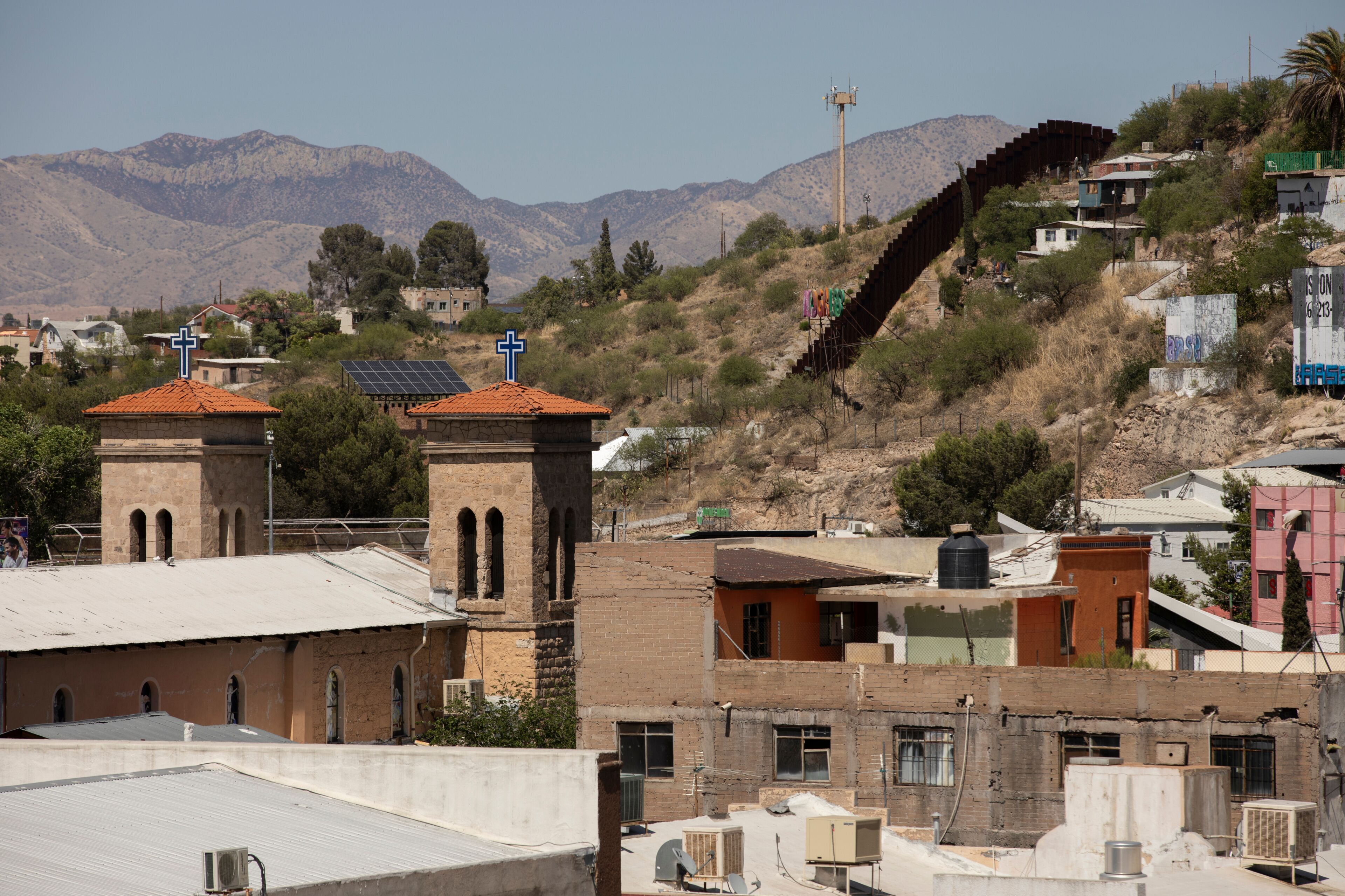 Afternoon sun shines on the historic downtown church in central Heroica Nogales, Sonora, Mexico, with the USA border wall in the distance.