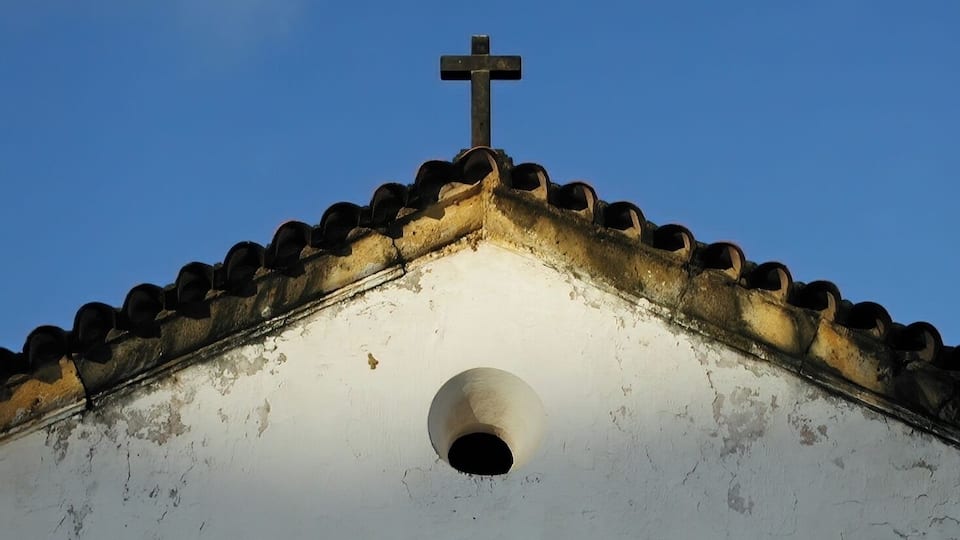 Un tetto di una chiesa con una croce e una finestra circolare.
