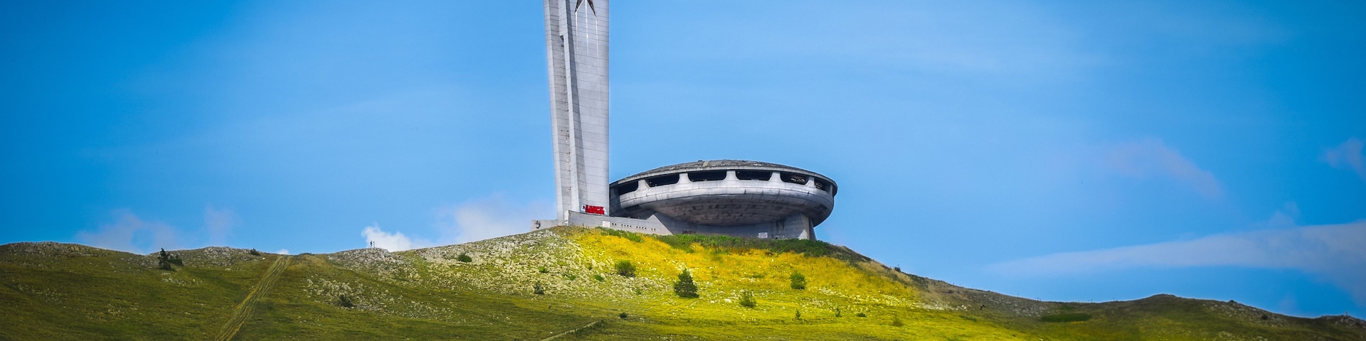 Un monumento cilíndrico grande con una estrella en la parte superior, ubicado en una colina cubierta de césped bajo un cielo azul despejado.