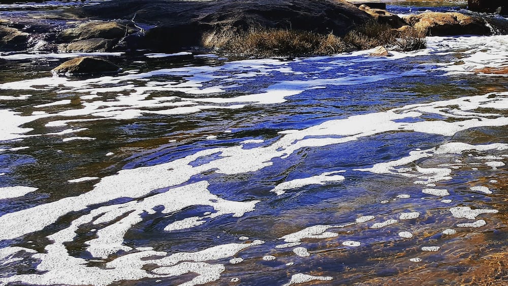 Ein Fluss mit klarem Wasser, vereisten Stellen und einem Wasserfall in bewaldeter Landschaft.