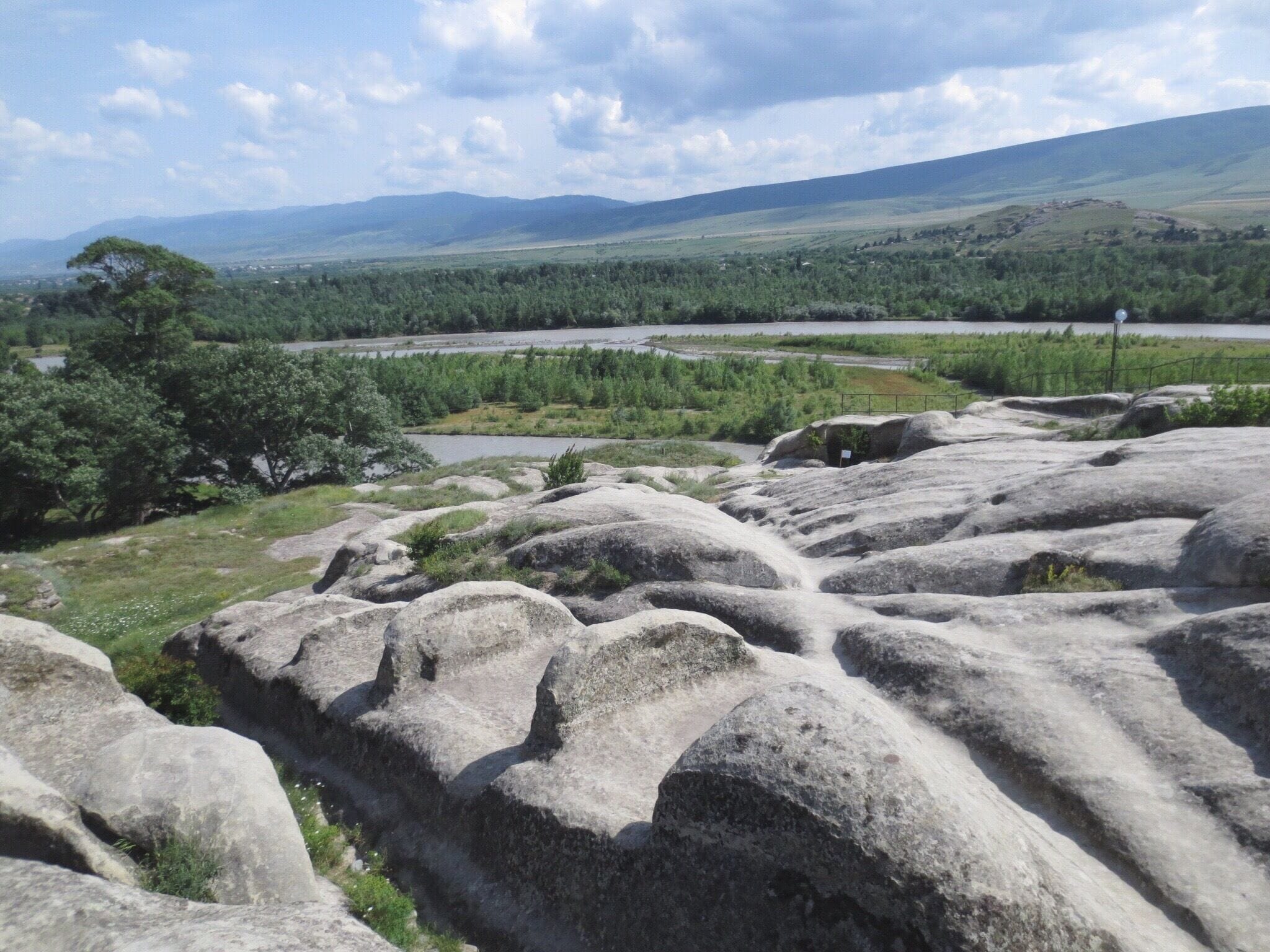 A rocky landscape with large boulders, a river, and distant hills.