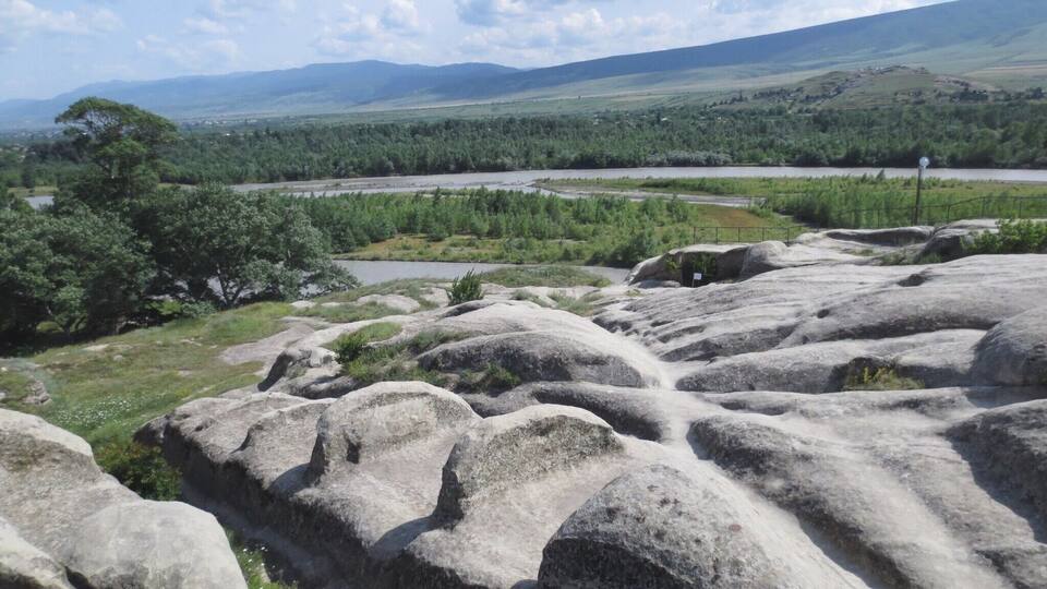 A rocky landscape with large boulders, a river, and distant hills.